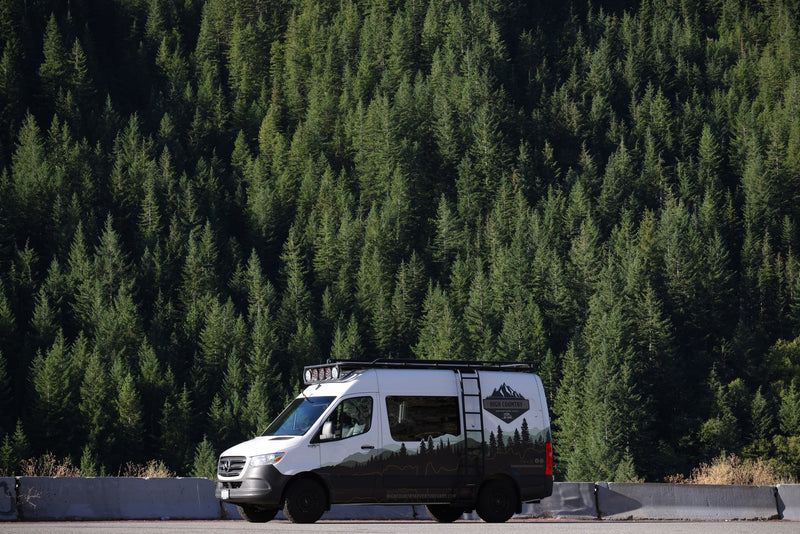 High Country Adventure RV rental van with mountain livery, parked beside a dense pine forest. — photo 10