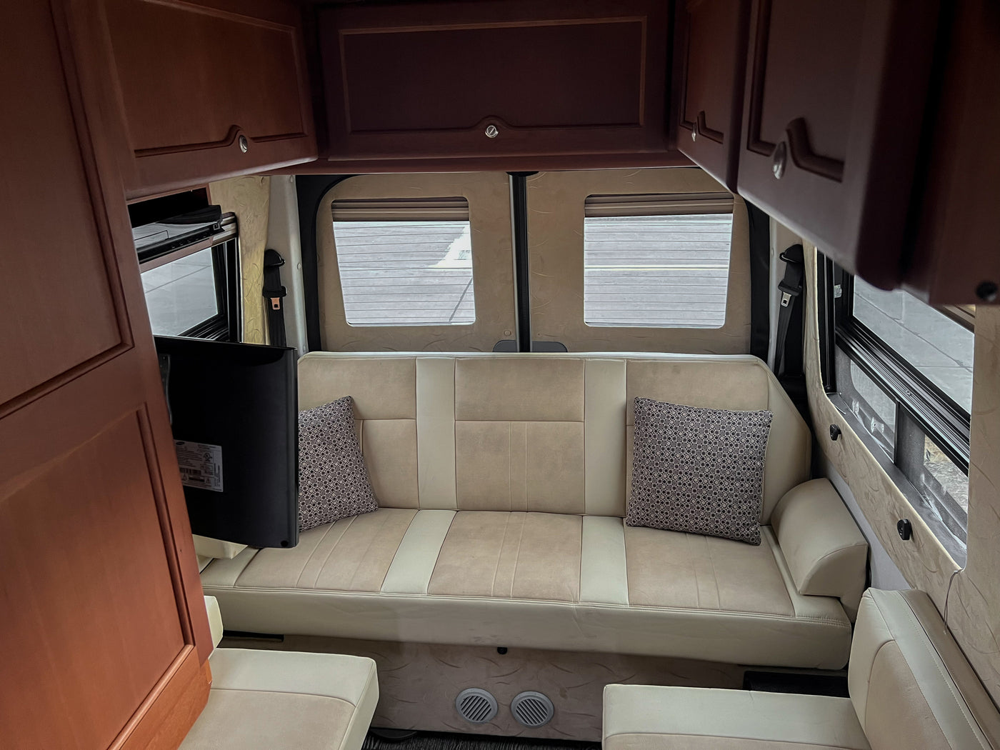This cozy RV rental interior features a beige sofa, overhead wooden cabinets, and a TV, perfect for relaxing. — photo 17