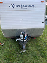 Front view of a white Sportsmen Classic RV rental (by KZ), showing its propane tank and hitch on green grass.
