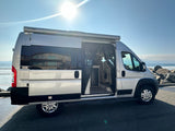 Silver RV rental van with open side door by the sunny ocean, perfect for coastal adventures.