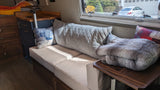 Cozy RV rental interior with sofa, patterned pillows, and a window view of a car and garage. Perfect for compact living.
