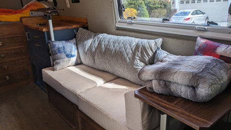 Cozy RV rental interior with sofa, patterned pillows, and a window view of a car and garage. Perfect for compact living.