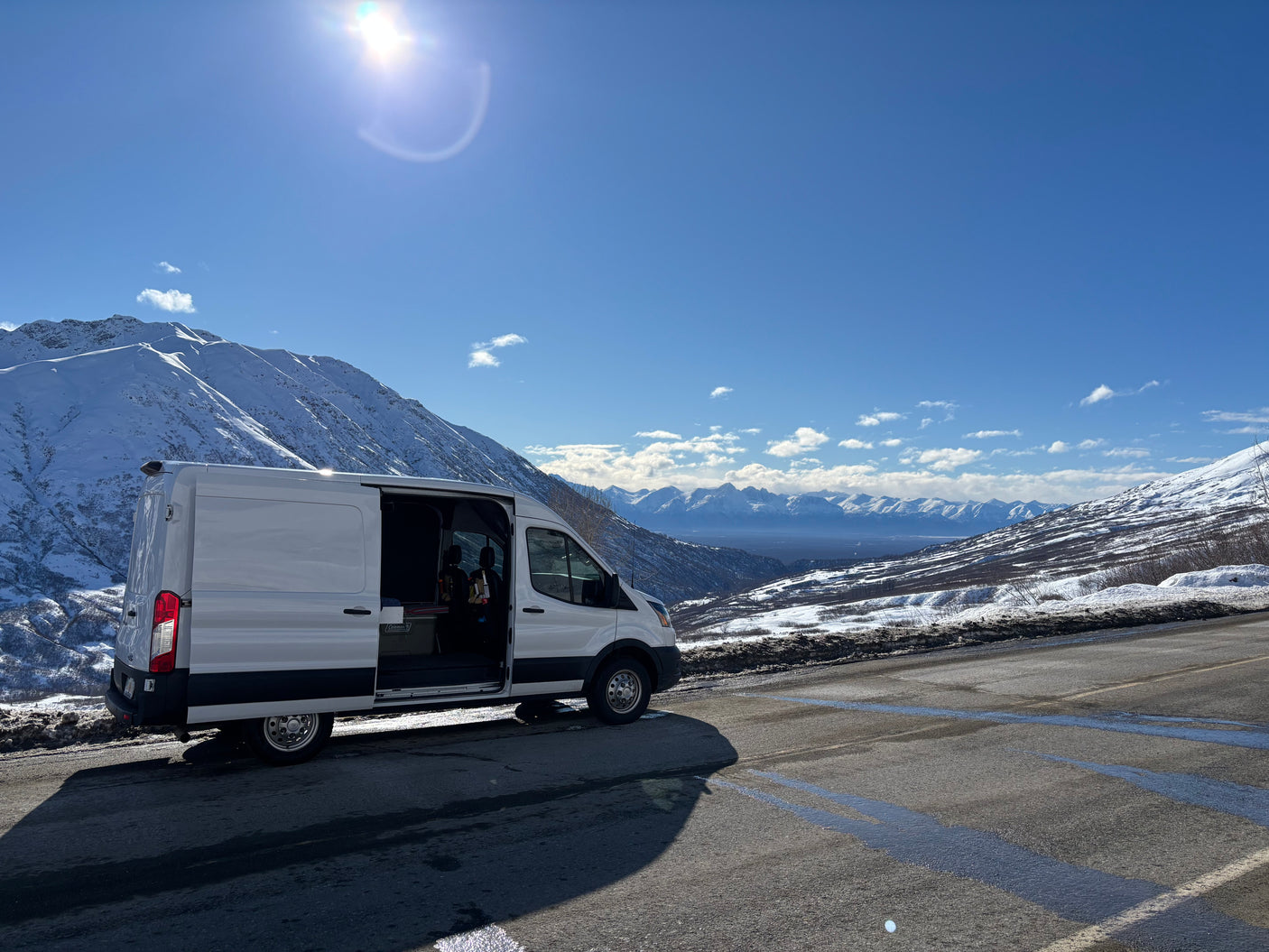 Scenic RV rental adventure! A white camper van parked on a snowy mountain road with stunning views. Perfect for a winter road trip.
