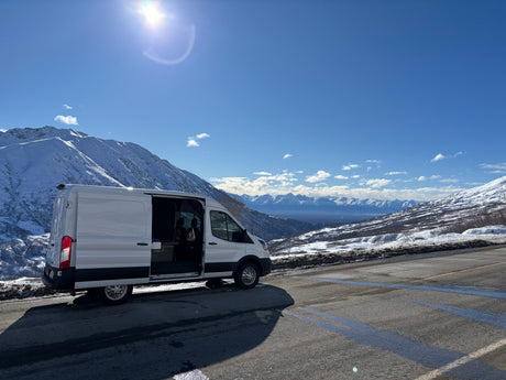 Scenic RV rental adventure! A white camper van parked on a snowy mountain road with stunning views. Perfect for a winter road trip.