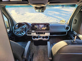 RV rental interior view: spacious driver's cockpit with dashboard, steering wheel, and front seats, parked on sandy terrain.
