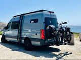 Adventure-ready gray RV rental, with fat-tire e-bikes and spare, parked by the ocean.