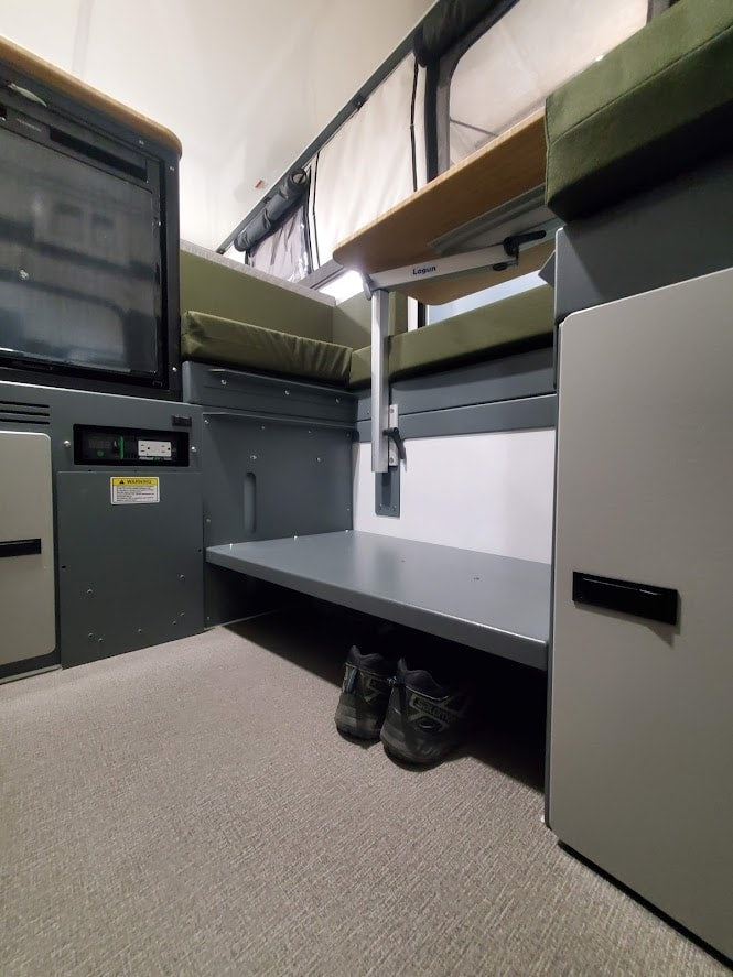 Modern RV rental interior with a pop-top roof, flexible Lagun table, fridge, and under-bench storage. Salomon shoes visible. — photo 2