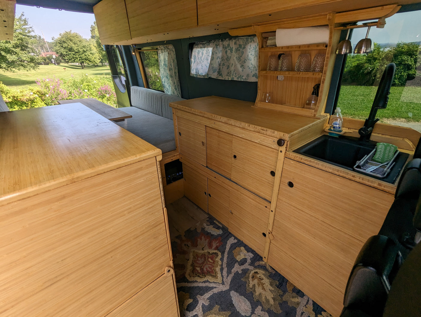 RV rental: Bamboo-finished camper van interior with kitchenette, upholstered seating, and scenic park views.