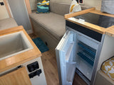 This RV rental interior features an open fridge, a sink, an induction cooktop, and a cozy seating area.