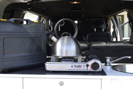 Compact camp kitchen in an rv rental: portable stove with kettle, storage case, and a small sink.
