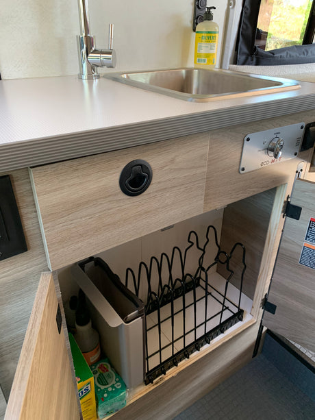 RV rental kitchen: stainless steel sink, eco-HOT water control, and under-counter storage with dish rack & cleaning supplies.