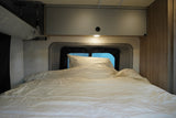 Cozy rv rental bedroom: a bed with white bedding, window, overhead cabinet, and light provide comfort for travel.