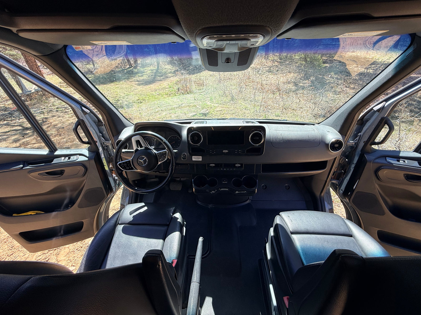 Spacious rv rental cabin view from rear, featuring dashboard, steering wheel, front seats, and open doors to nature.