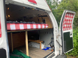 Interior of a converted RV rental van, featuring a cozy bed with red/white checkered bedding, under-bed storage, and power setup.