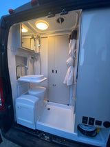 Inside an RV rental: a compact wet bath with toilet, sink, shower, mirror, and controls for a comfortable mobile setup.