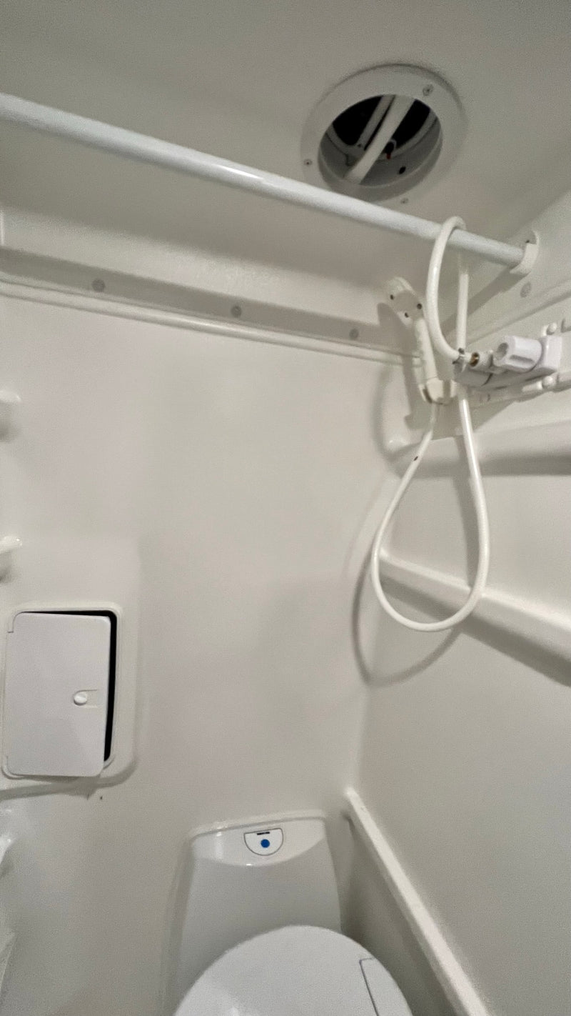 Inside this compact RV rental bathroom: an all-white design with a toilet, handheld shower, and ceiling vent. — photo 2