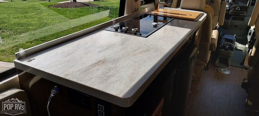 Inside a bright RV rental kitchen: modern countertop, built-in cooktop, and sink area with outdoor view.