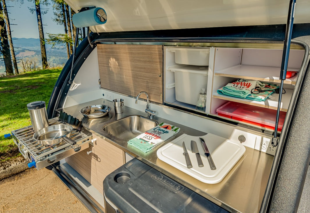 This RV rental's teardrop outdoor kitchen features a sink, slide-out stove, cooler, and storage.