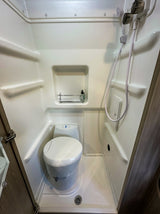 Inside an RV rental: a compact wet bath with a toilet, shower head, and floor drain, ideal for camper travel.