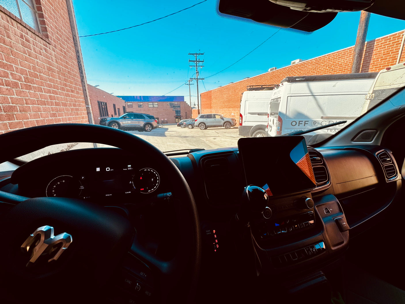 Driver's view from a Ram RV rental dashboard (30k miles), with "Off Grid Travel" vans parked outside in a sunny lot.