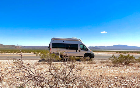 Silver RV rental parked on a desert road with mountains under a clear blue sky, ideal for your next adventure.
