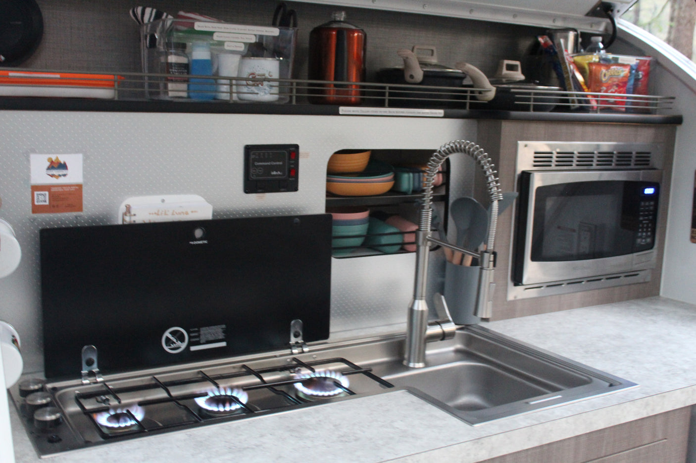 Fully equipped RV rental kitchen: gas stove with active burners, pull-down sink faucet, microwave, and organized storage.