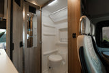 Interior of a modern RV rental, featuring a compact bathroom with toilet and shower, next to stylish wooden panels and seating.