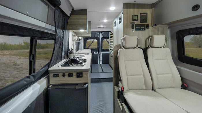 Inside this modern rv rental, see the compact kitchen, comfortable seating, and a view of nature outside.
