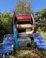 This RV rental features a cozy bed, Igloo cooler, & Tommy Bahama chairs, perfect for outdoor travel.