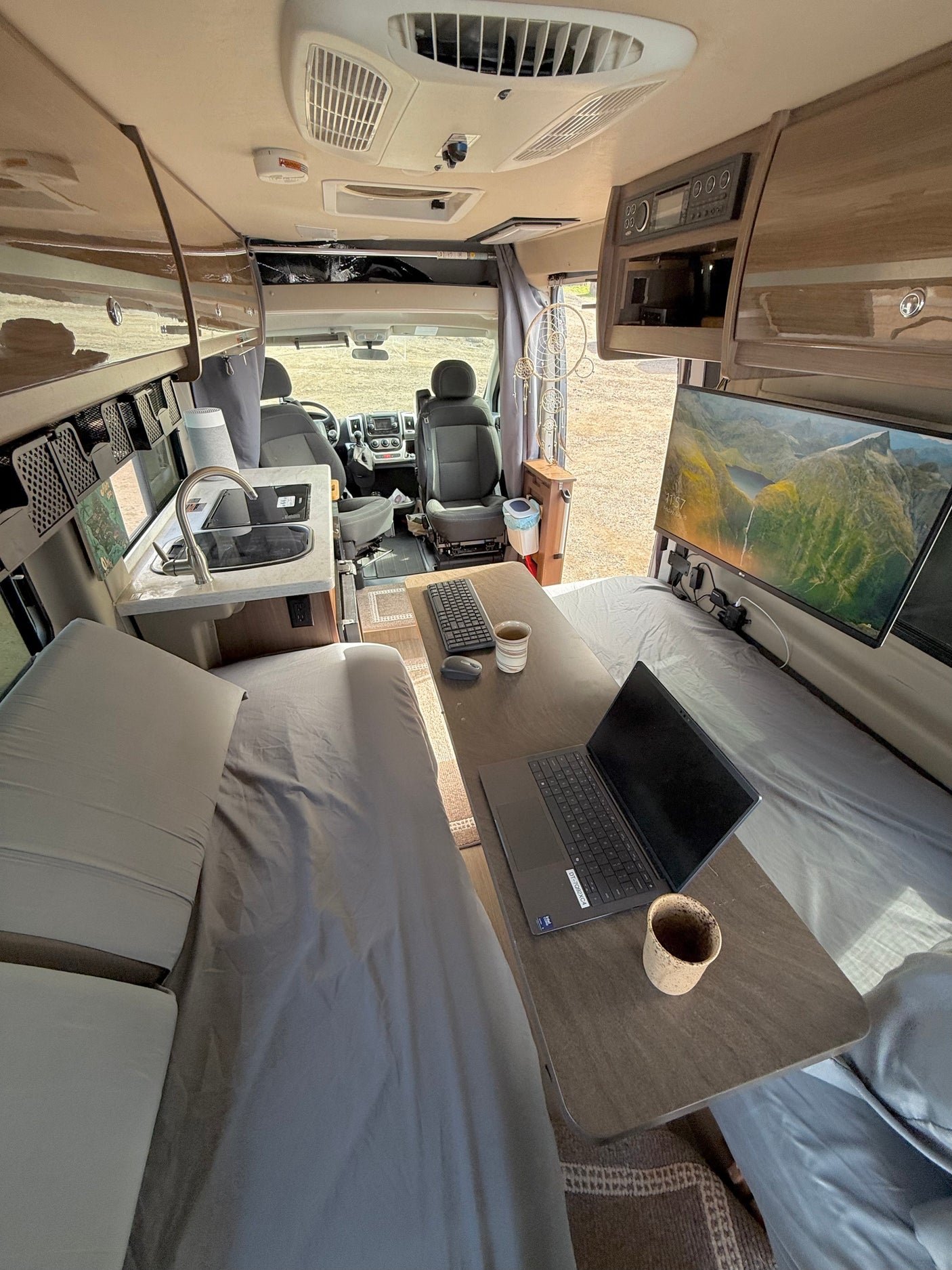 RV rental interior: A bright, functional mobile office and living space with kitchen, beds, laptop, and ultrawide monitor workstation.