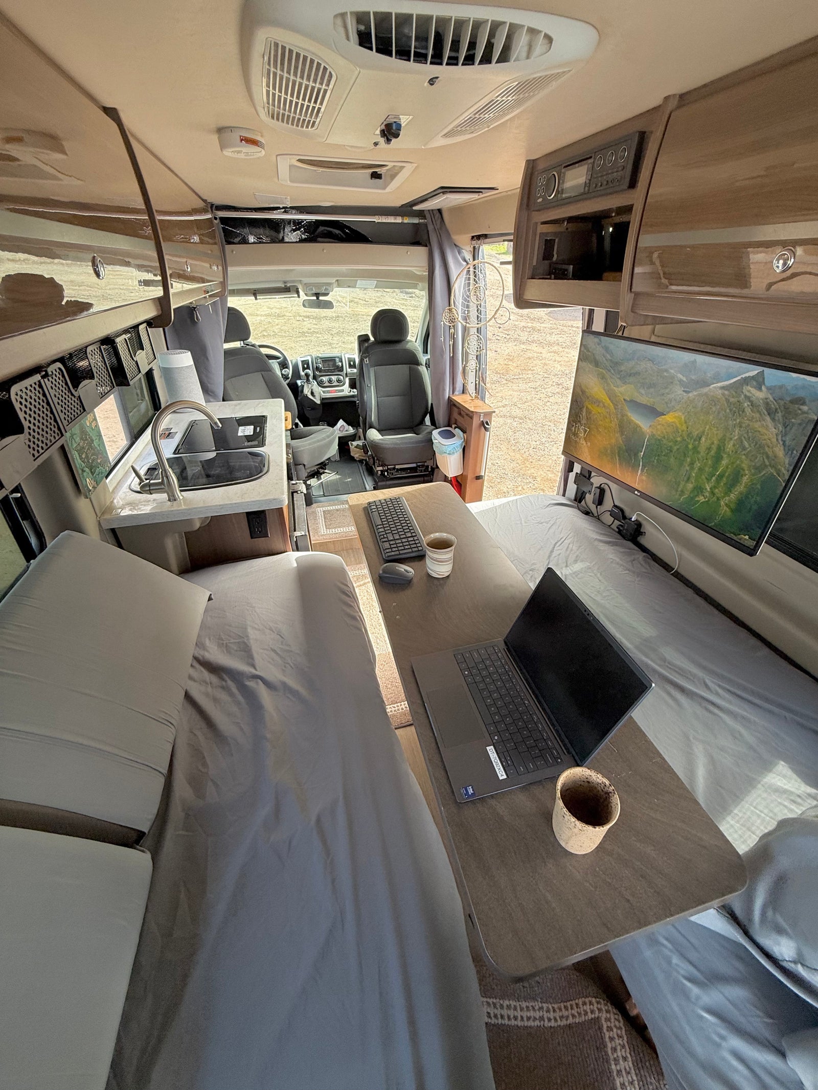 RV rental interior: A bright, functional mobile office and living space with kitchen, beds, laptop, and ultrawide monitor workstation.