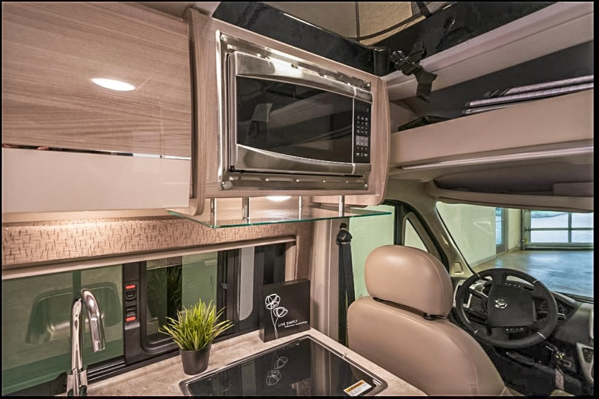 This RV rental features a compact kitchen with a microwave, sink, and a view into the front driving cabin.