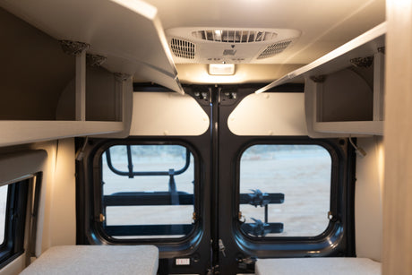 Interior view of an rv rental, showcasing overhead storage, a ceiling AC unit, and rear windows with an external rack.