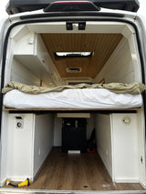 RV rental: Back of a customized camper van featuring an elevated bed, wood-paneled ceiling, and large under-bed storage.