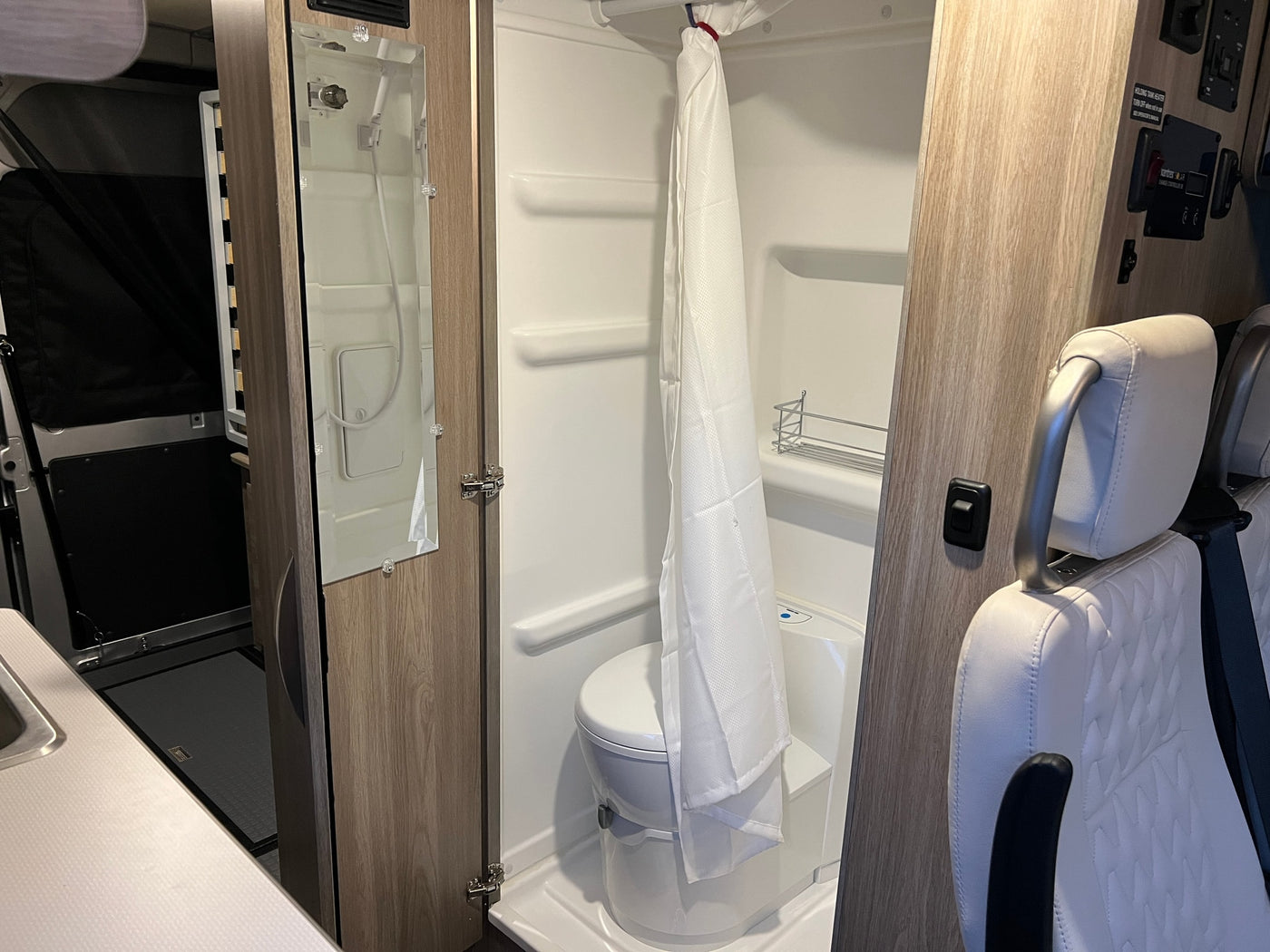 Inside an RV rental: full wet bath (toilet, shower, mirror), compact kitchen, and front seats. Efficient use of space for your trip. — photo 6