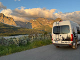 White Mercedes Sprinter rv rental van overlooking scenic mountains, lake, & forest at golden hour.