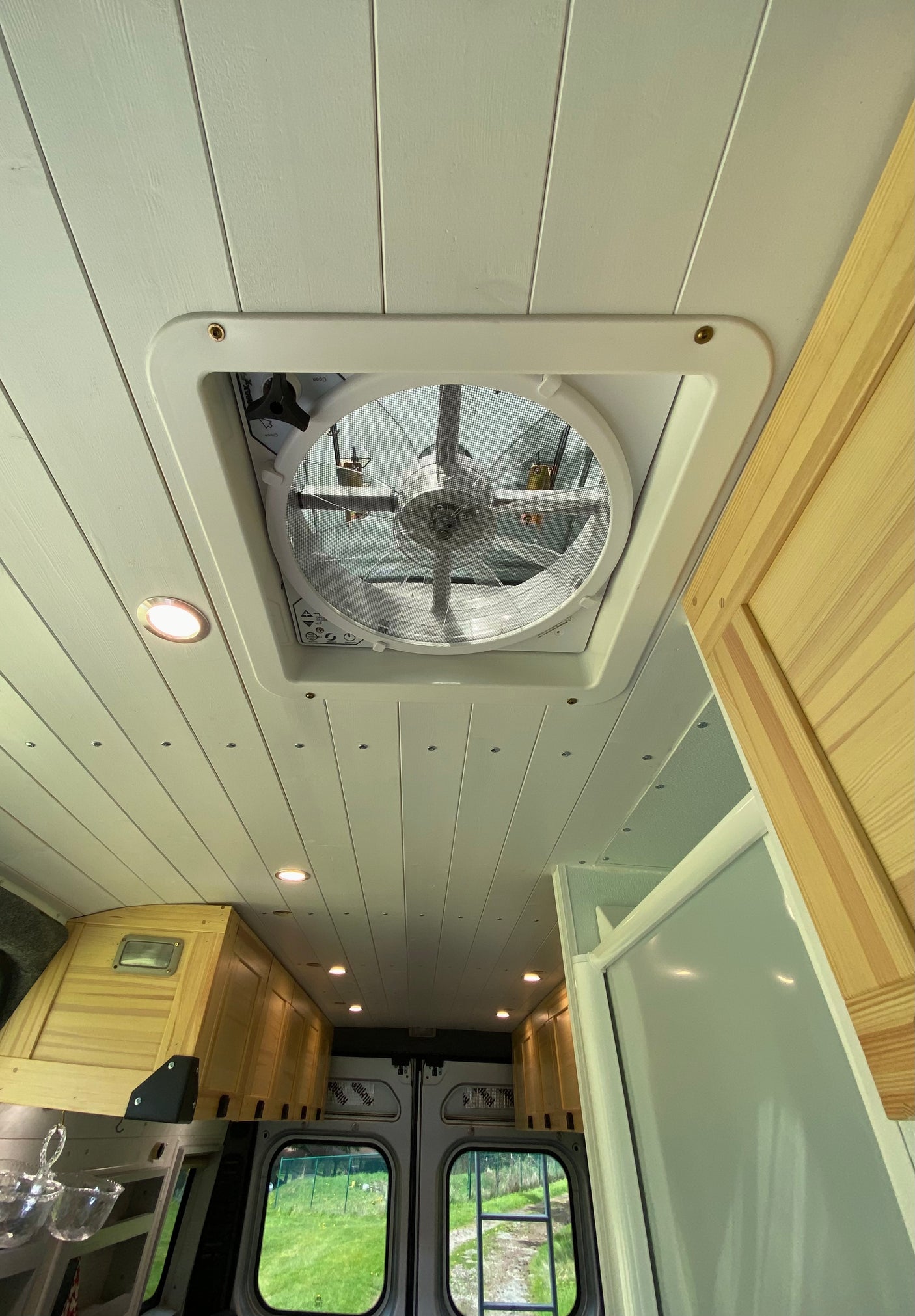 Looking up at a modern RV rental ceiling with a white slatted design, a large central vent fan, and recessed LED lights.