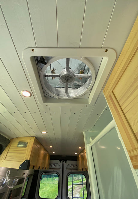 Looking up at a modern RV rental ceiling with a white slatted design, a large central vent fan, and recessed LED lights.