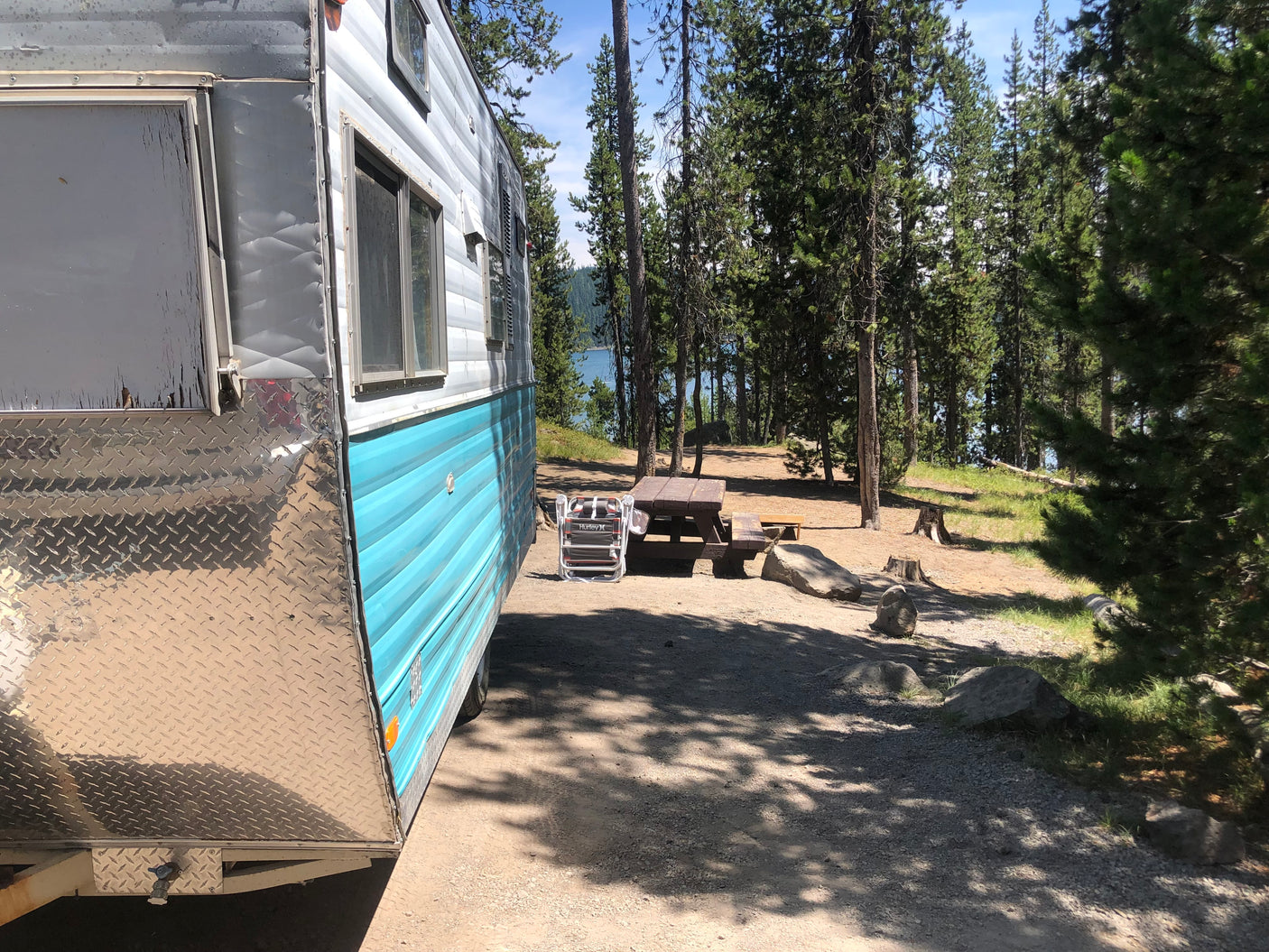 Enjoying nature with this blue and silver rv rental at a wooded lakeside campsite, complete with picnic table.