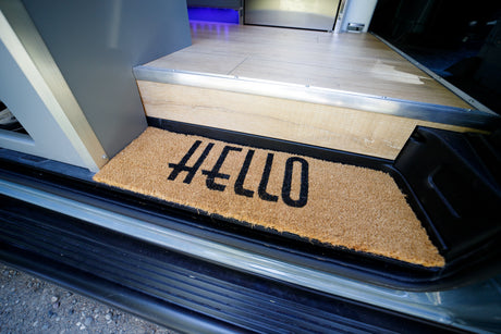 Cozy RV rental entrance: a welcoming 'HELLO' doormat on the custom wood-look floor step.