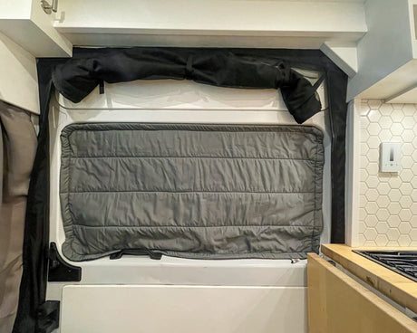RV rental interior: window with insulated grey shade, rolled-up black cover, hexagonal tile backsplash, & kitchen counter.