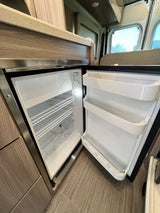 Open Vitrifrigo fridge in an RV rental, showcasing its spacious interior with shelves and door bins for fresh food storage.