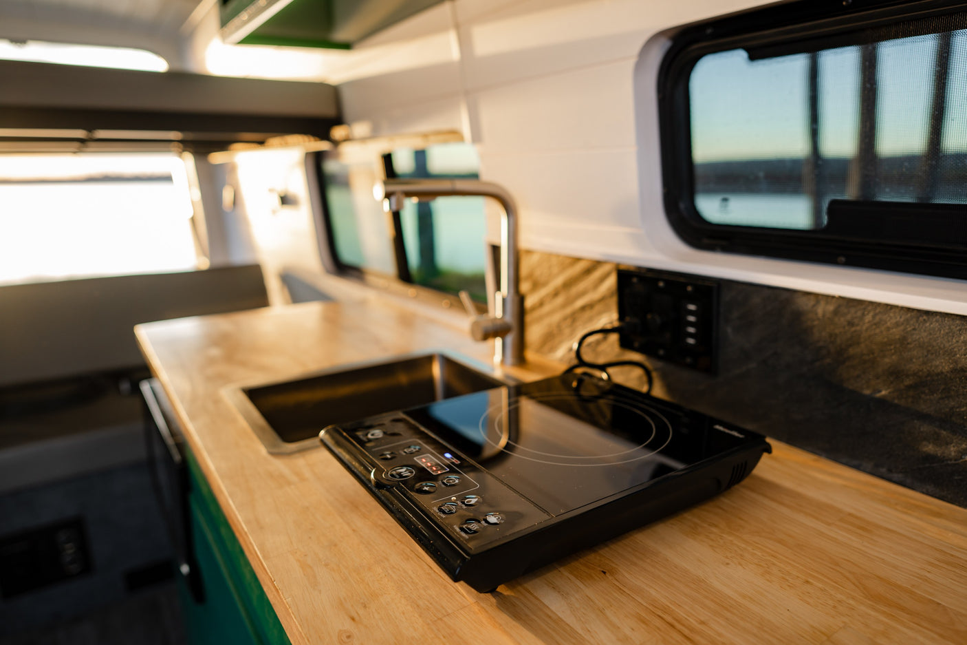 RV rental kitchen: Wood countertop, sink, and portable induction cooktop with window views, ready for your adventure.