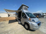 Spacious silver pop-top RV rental camper van with extended awning and open side door, ready for adventure.
