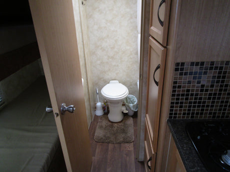 Inside an RV rental: a compact bathroom with toilet, comfortable bed area, and efficient kitchen with stovetop & cabinets.