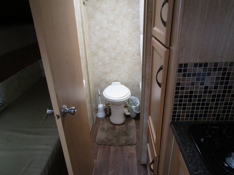 Inside an RV rental: a compact bathroom with toilet, comfortable bed area, and efficient kitchen with stovetop & cabinets. — photo 8