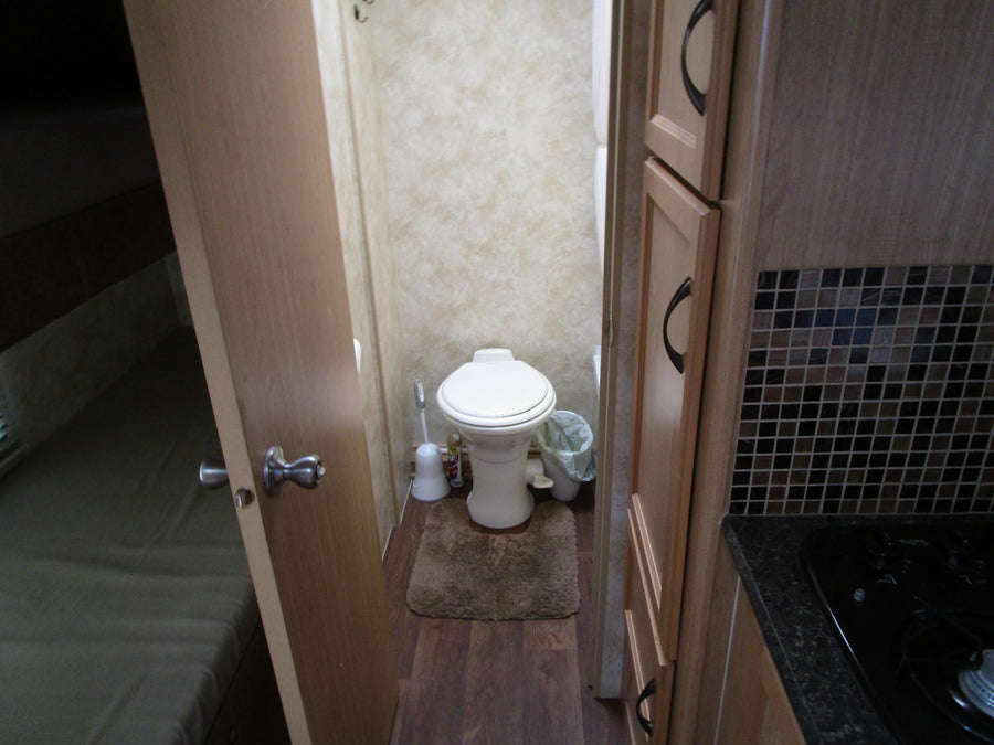 Inside an RV rental: a compact bathroom with toilet, comfortable bed area, and efficient kitchen with stovetop & cabinets.