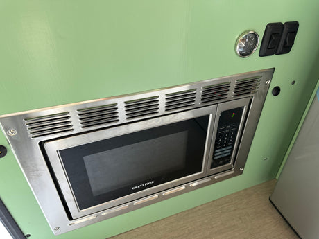 Greystone microwave, water gauge, and switches on a green panel, showcasing an RV rental interior's amenities.