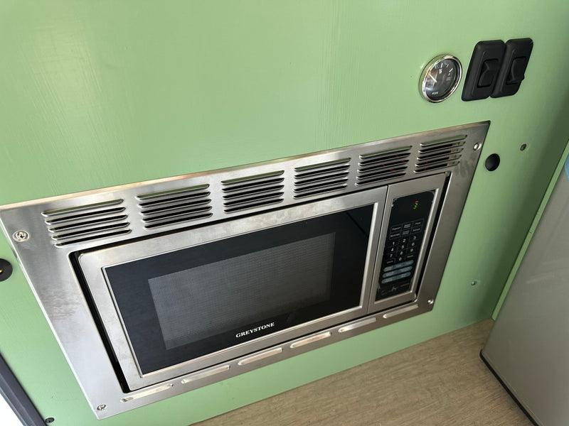 Greystone microwave, water gauge, and switches on a green panel, showcasing an RV rental interior's amenities. — photo 8