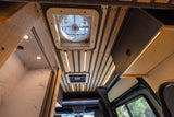 Stylish RV rental interior with wood-slat ceiling, LED lights, skylight, tiled shower & overhead storage.